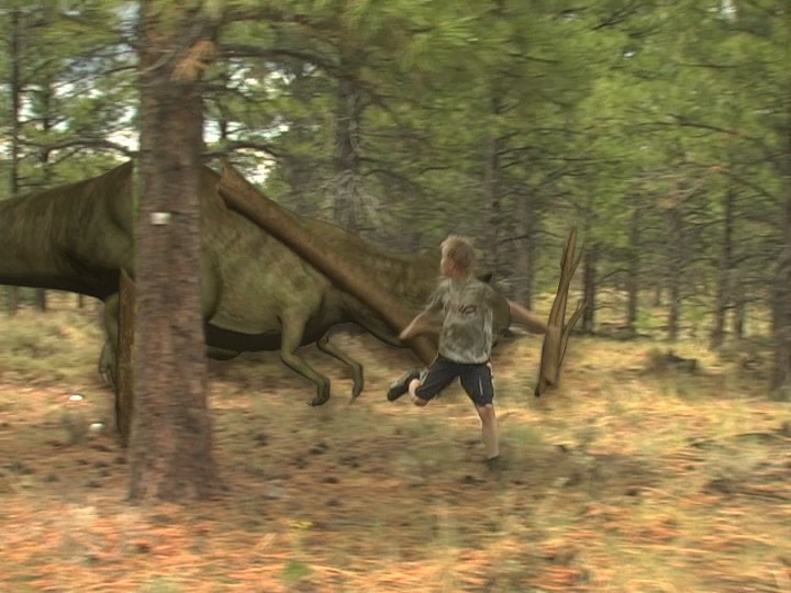 A CG tyrannosaur chases a running boy through a pine forest in old video footage, passing behind a tree
