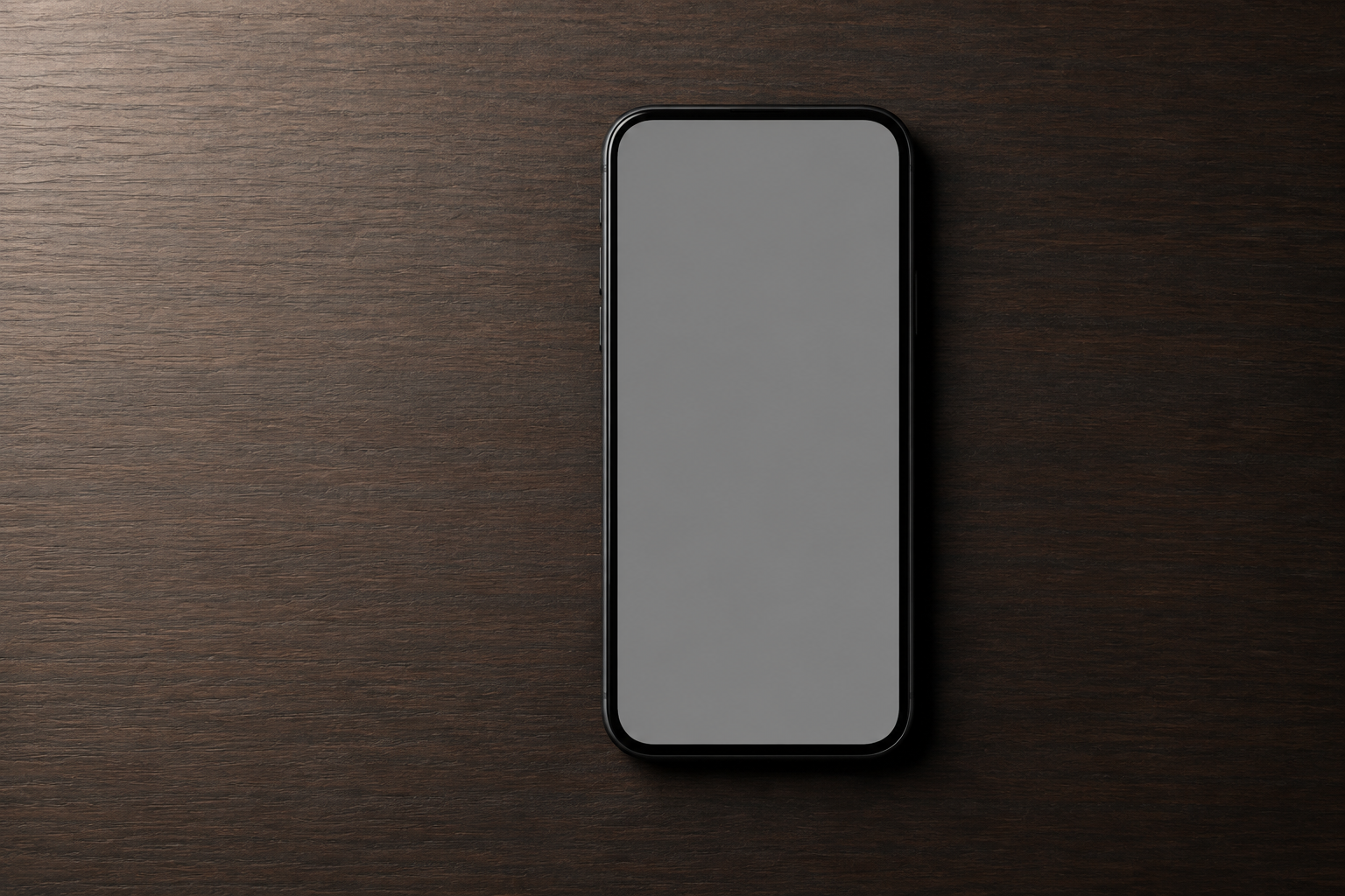 Phone on a dark wooden desk with a blank gray screen